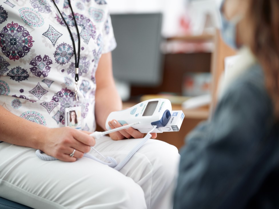 Nurse or clinician measures a patient's blood pressure using a digital monitor in a clinic setting, cuff on the arm and device in hand.
