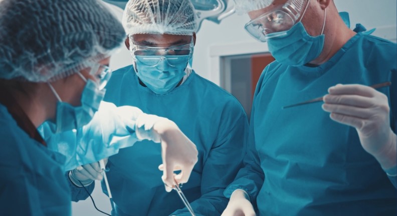 smoke2 Three surgeons in blue scrubs, masks, and gloves perform an operation in a bright operating room.