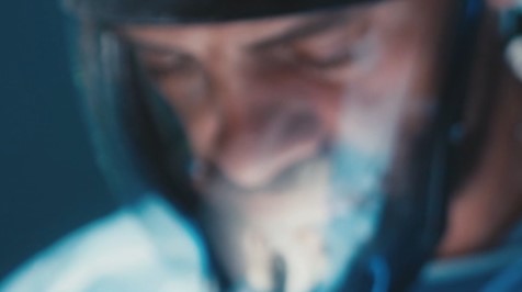 smoke3 Close-up of a person wearing a helmet and headset, face out of focus with a blue-lit background.
