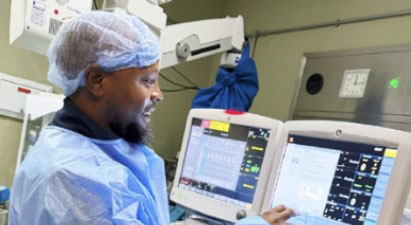 BAN2 Healthcare worker in blue scrubs and hairnet operating patient monitors in a hospital ICU.