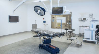 useBAN3 Modern operating room with an empty surgical table, overhead light, monitors, and anesthesia equipment surrounding it.